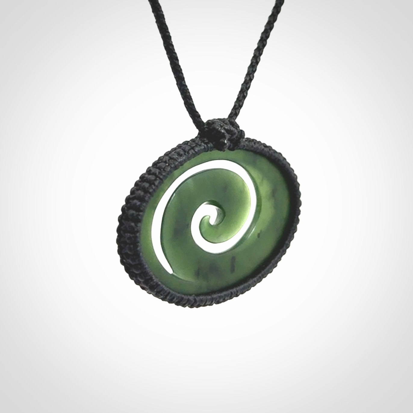 This picture shows a medium sized hand carved jade koru pendant. It is a darker green colour which is quite translucent where the jade is thin. The cord is bound in a macrame style and is adjustable so that you can position the pendant where it suits you best.