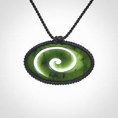This picture shows a medium sized hand carved jade koru pendant. It is a darker green colour which is quite translucent where the jade is thin. The cord is bound in a macrame style and is adjustable so that you can position the pendant where it suits you best.