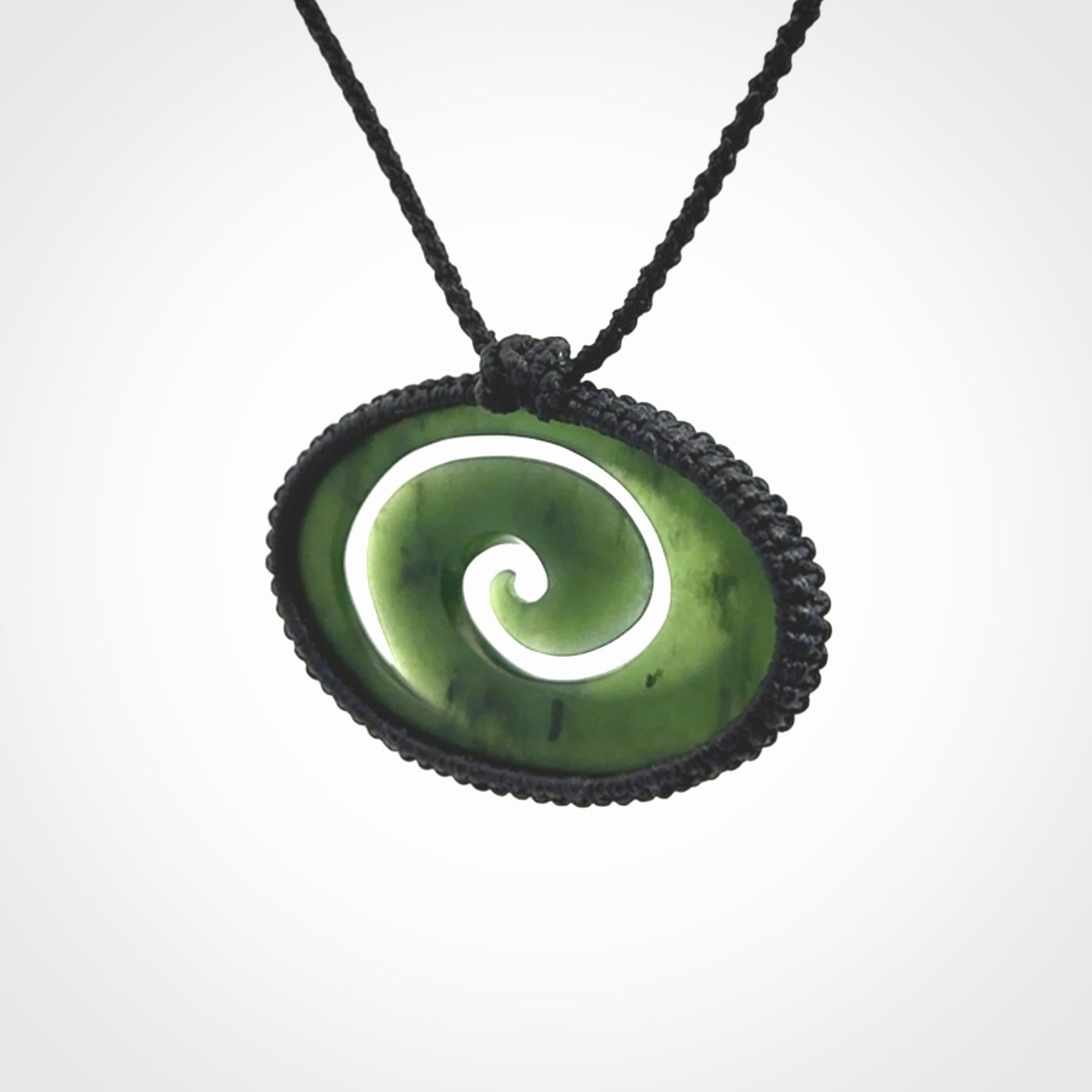 This picture shows a medium sized hand carved jade koru pendant. It is a darker green colour which is quite translucent where the jade is thin. The cord is bound in a macrame style and is adjustable so that you can position the pendant where it suits you best.