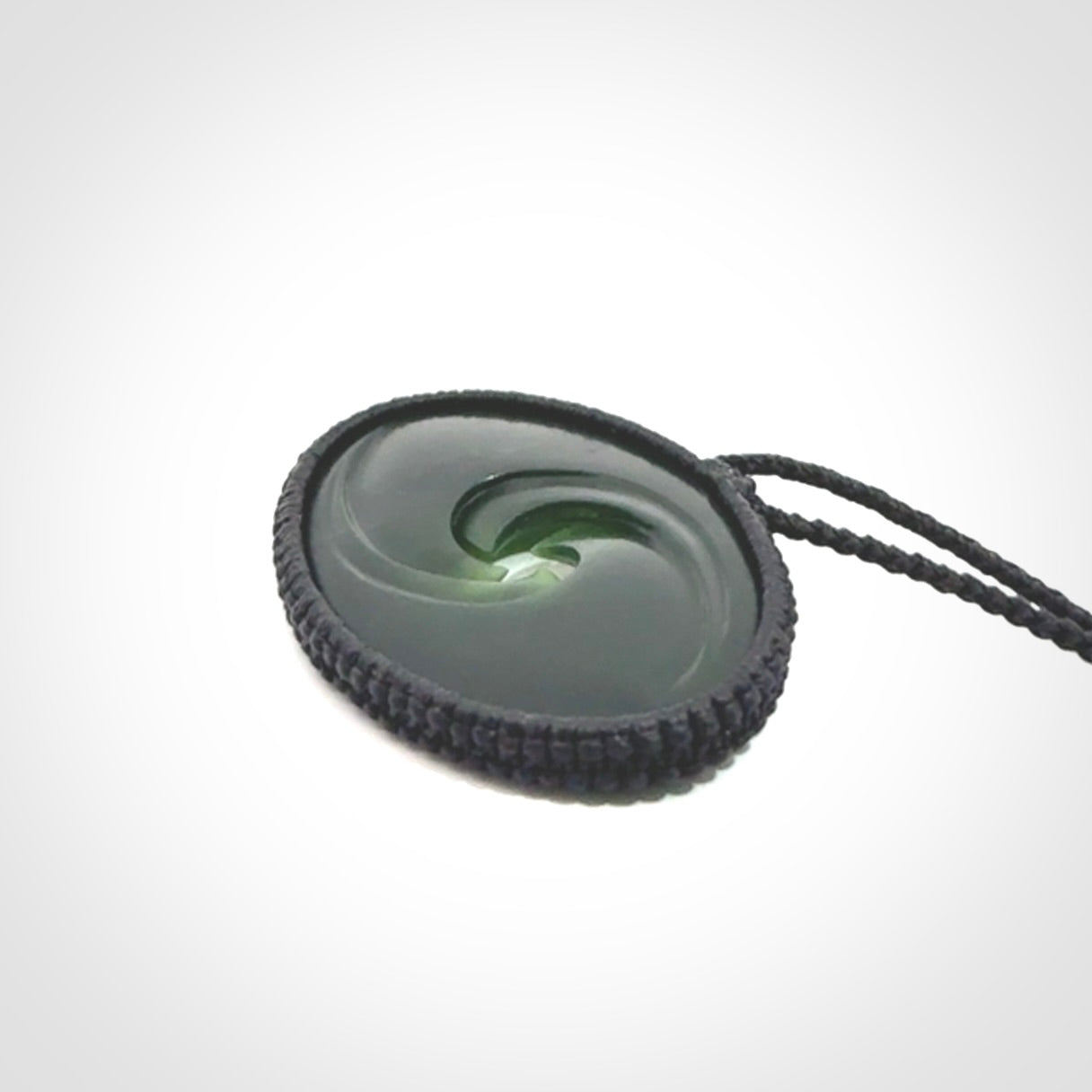 This picture shows a medium sized hand carved jade koru pendant. It is a darker green colour which is quite translucent where the jade is thin. The cord is bound in a macrame style and is adjustable so that you can position the pendant where it suits you best.