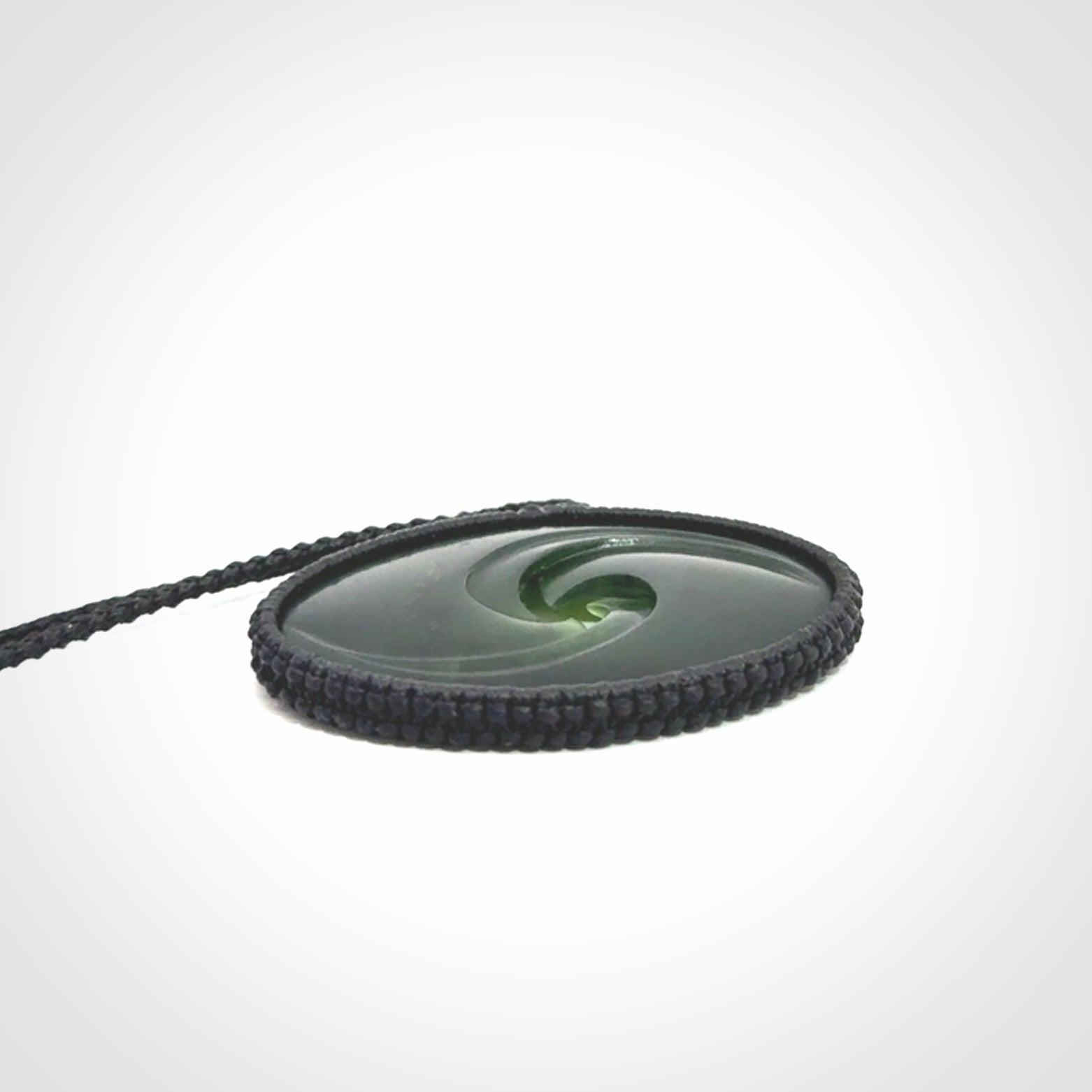 This picture shows a medium sized hand carved jade koru pendant. It is a darker green colour which is quite translucent where the jade is thin. The cord is bound in a macrame style and is adjustable so that you can position the pendant where it suits you best.