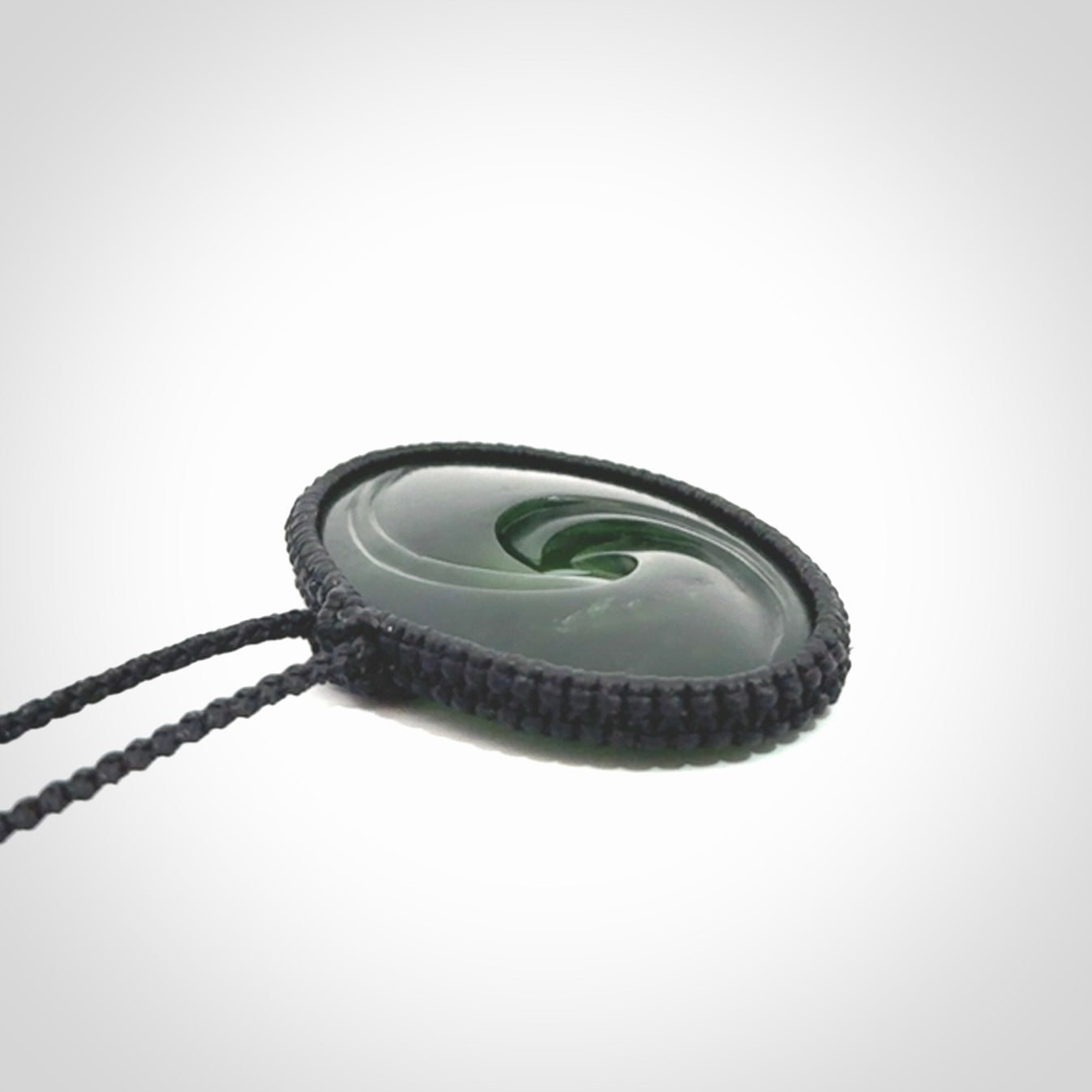 This picture shows a medium sized hand carved jade koru pendant. It is a darker green colour which is quite translucent where the jade is thin. The cord is bound in a macrame style and is adjustable so that you can position the pendant where it suits you best.