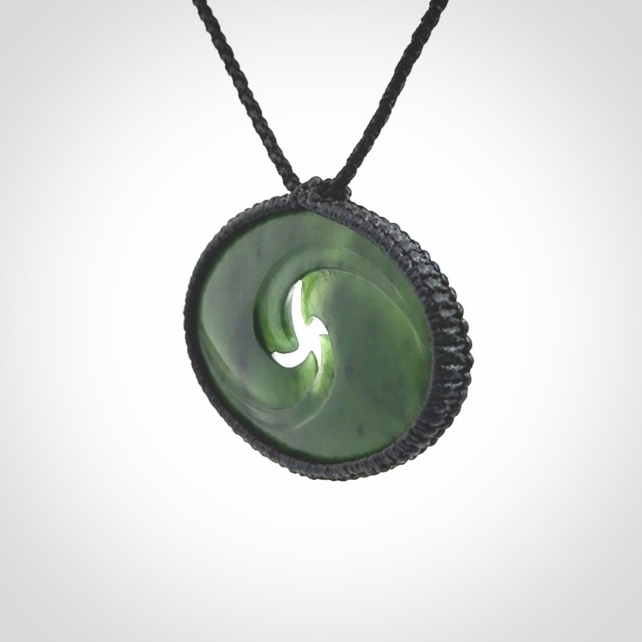 This picture shows a medium sized hand carved jade koru pendant. It is a darker green colour which is quite translucent where the jade is thin. The cord is bound in a macrame style and is adjustable so that you can position the pendant where it suits you best.