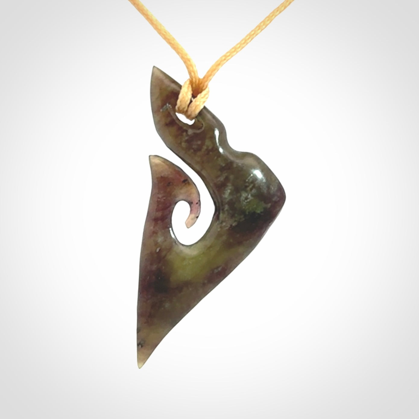 This photo shows a matau, hook, pendant carved from New Zealand Totoweka Pounamu, Jade. We provide this piece with an adjustable beige coloured cord.