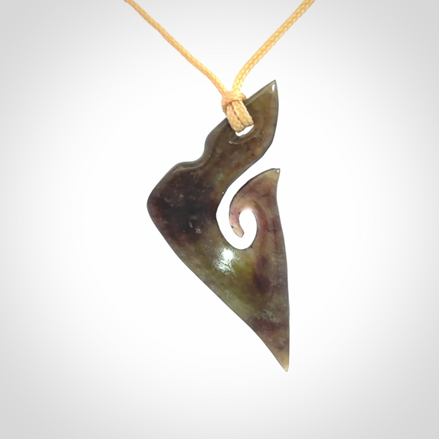 This photo shows a matau, hook, pendant carved from New Zealand Totoweka Pounamu, Jade. We provide this piece with an adjustable beige coloured cord.