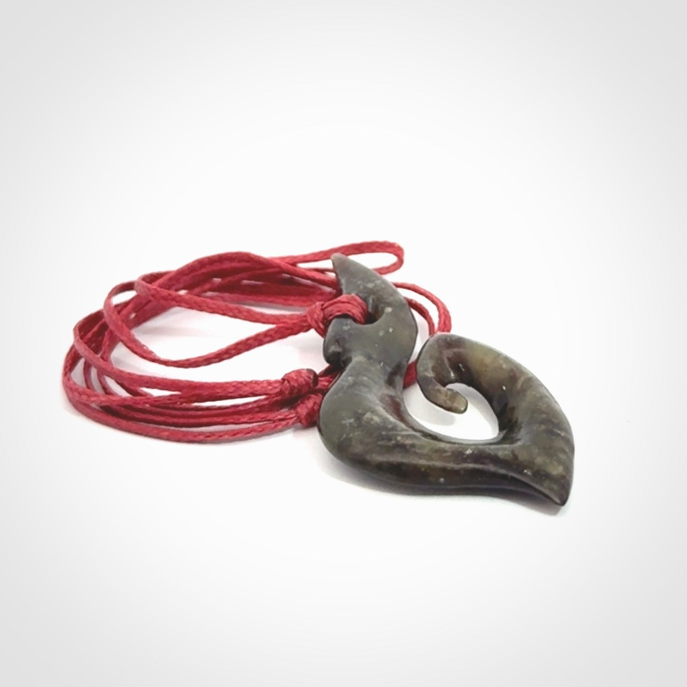 This photo shows a contemporary koru pendant carved from New Zealand Totoweka Jade. We provide this piece with an adjustable red cord.