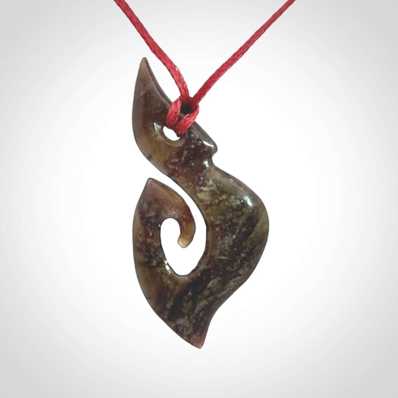 This photo shows a contemporary koru pendant carved from New Zealand Totoweka Jade. We provide this piece with an adjustable red cord.