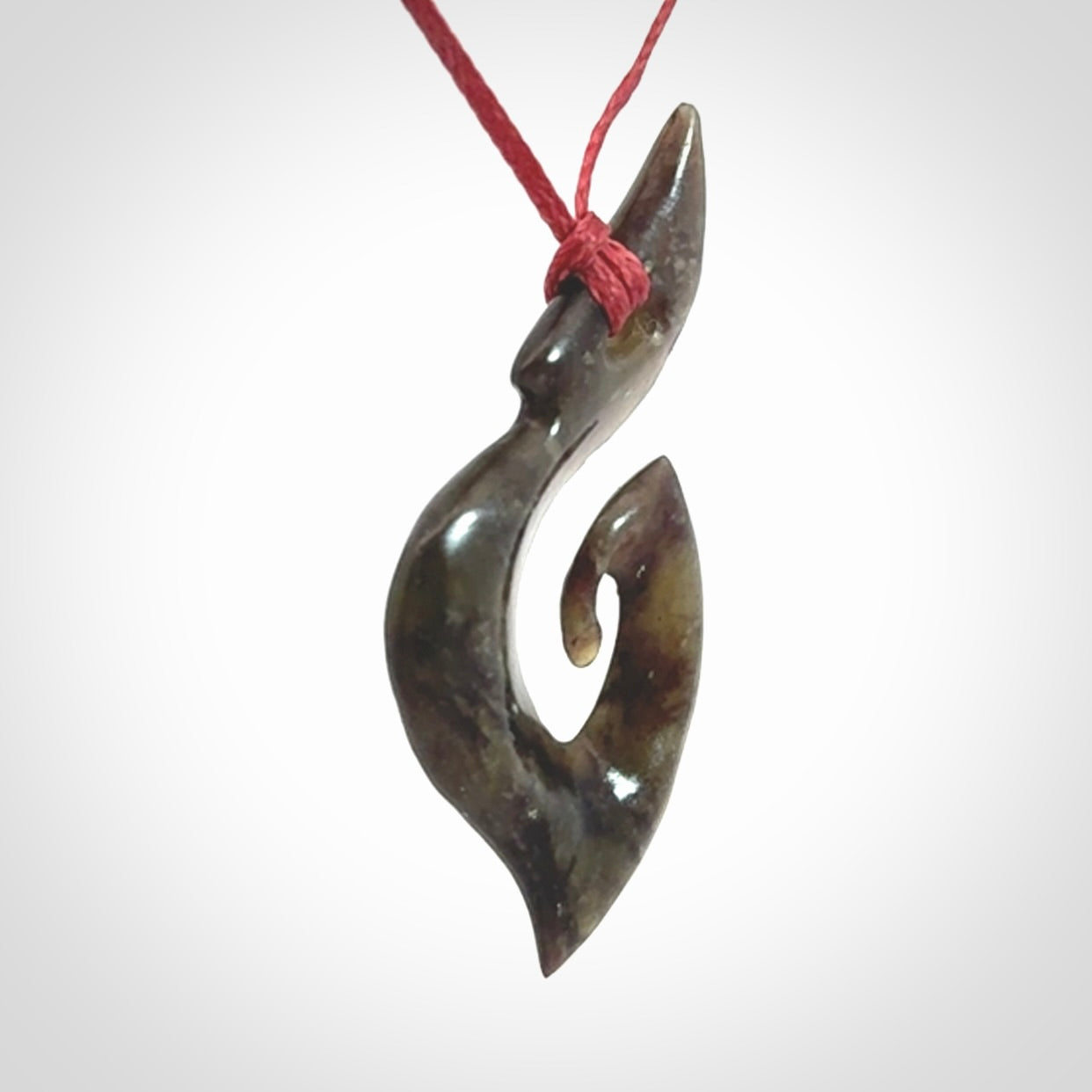 This photo shows a contemporary koru pendant carved from New Zealand Totoweka Jade. We provide this piece with an adjustable red cord.