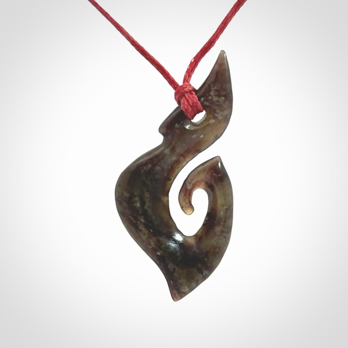 This photo shows a contemporary koru pendant carved from New Zealand Totoweka Jade. We provide this piece with an adjustable red cord.
