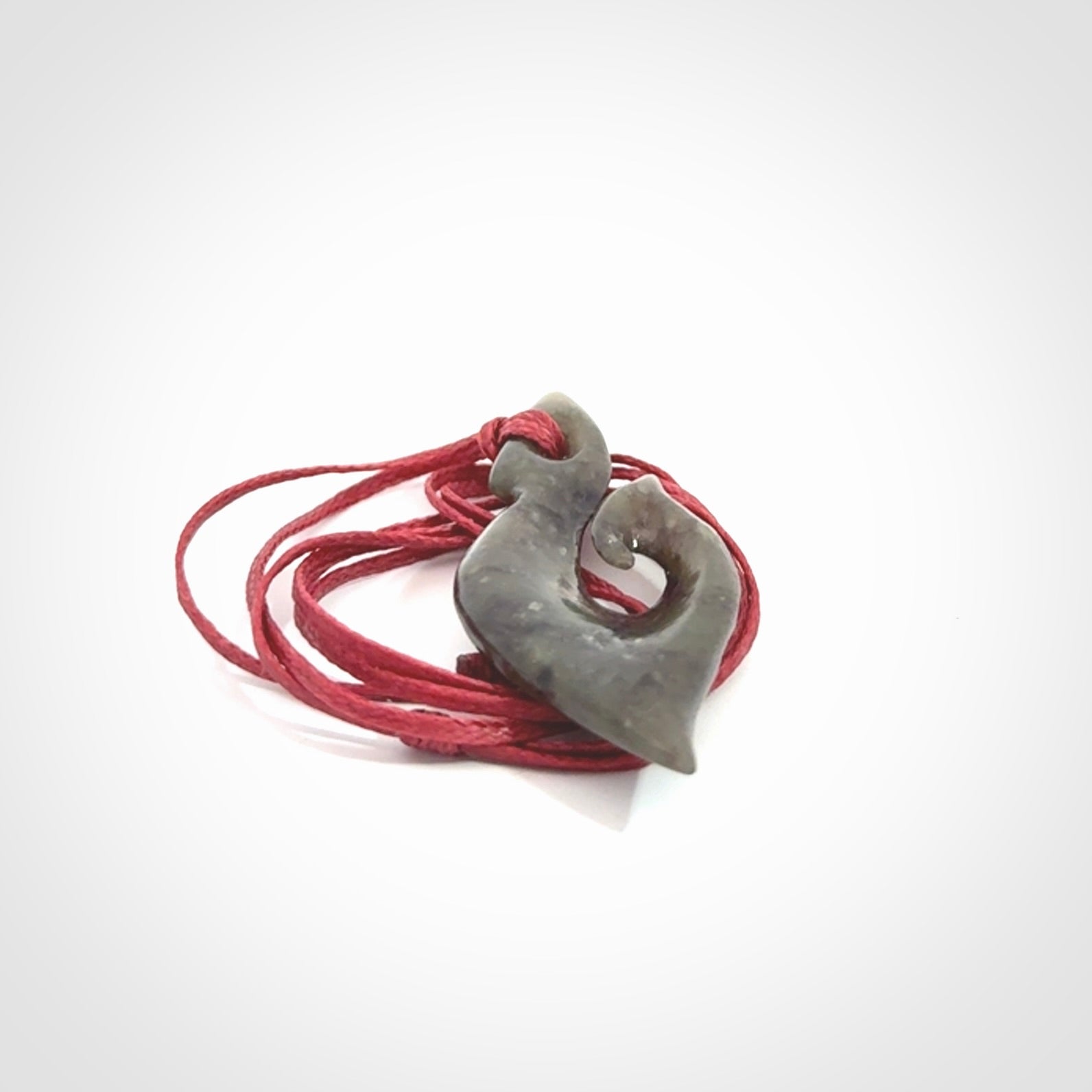 This photo shows a contemporary koru pendant carved from New Zealand Totoweka Jade. We provide this piece with an adjustable red cord.