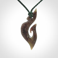 This photo shows a matau, hook, pendant carved from New Zealand Totoweka Pounamu, Jade. We provide this piece with an adjustable green coloured cord.