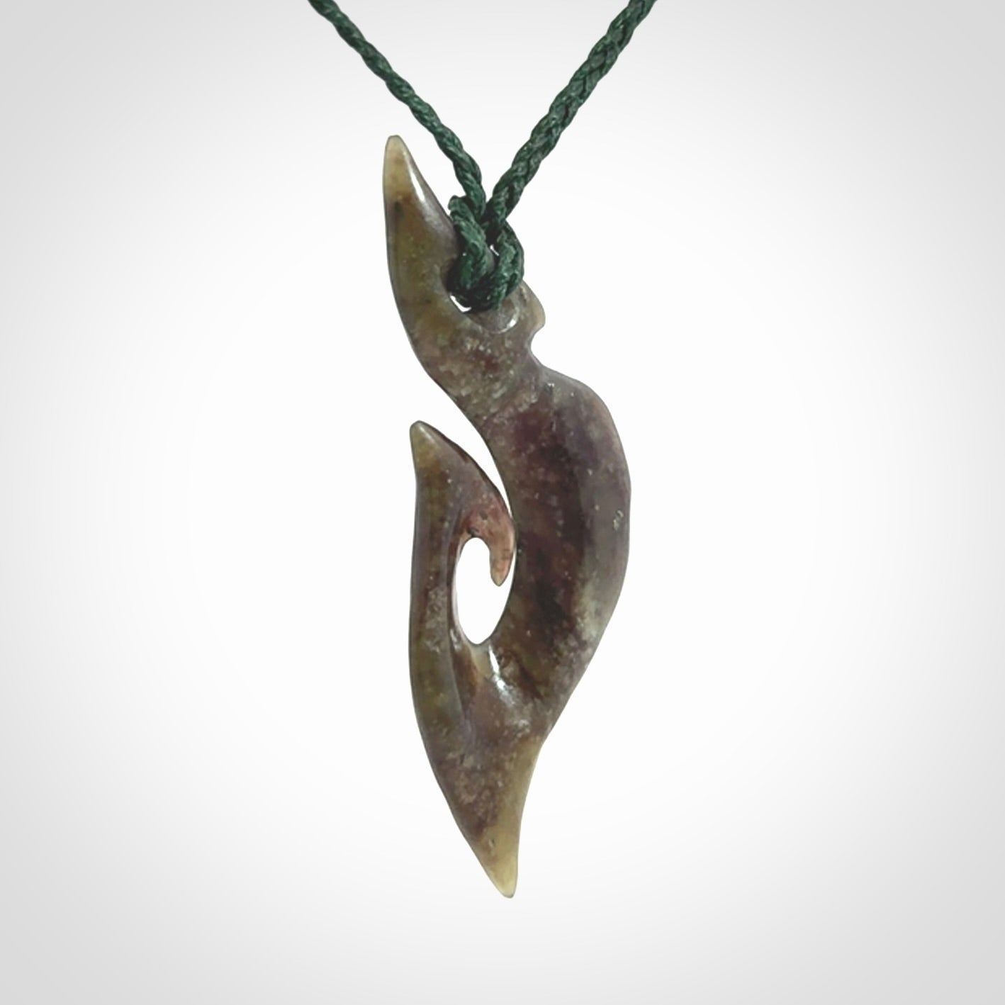 This photo shows a matau, hook, pendant carved from New Zealand Totoweka Pounamu, Jade. We provide this piece with an adjustable green coloured cord.