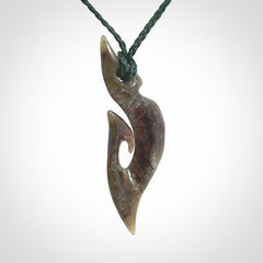 This photo shows a matau, hook, pendant carved from New Zealand Totoweka Pounamu, Jade. We provide this piece with an adjustable green coloured cord.