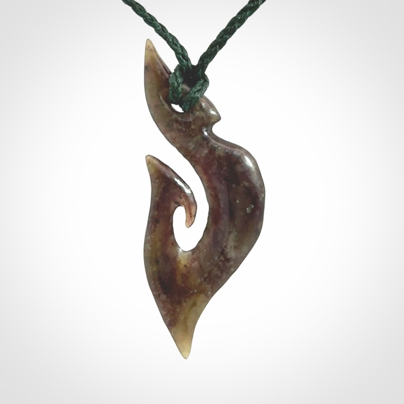 This photo shows a matau, hook, pendant carved from New Zealand Totoweka Pounamu, Jade. We provide this piece with an adjustable green coloured cord.
