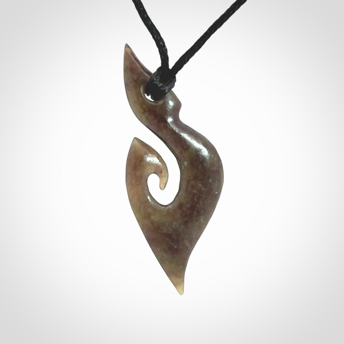 This photo shows a contemporary koru pendant carved from New Zealand Totoweka Jade. We provide this piece with a black fixed length cord.