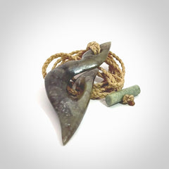 This photo shows a matau, hook, pendant carved from New Zealand Totoweka Pounamu, Jade. We provide this piece with an tan fixed length cord.