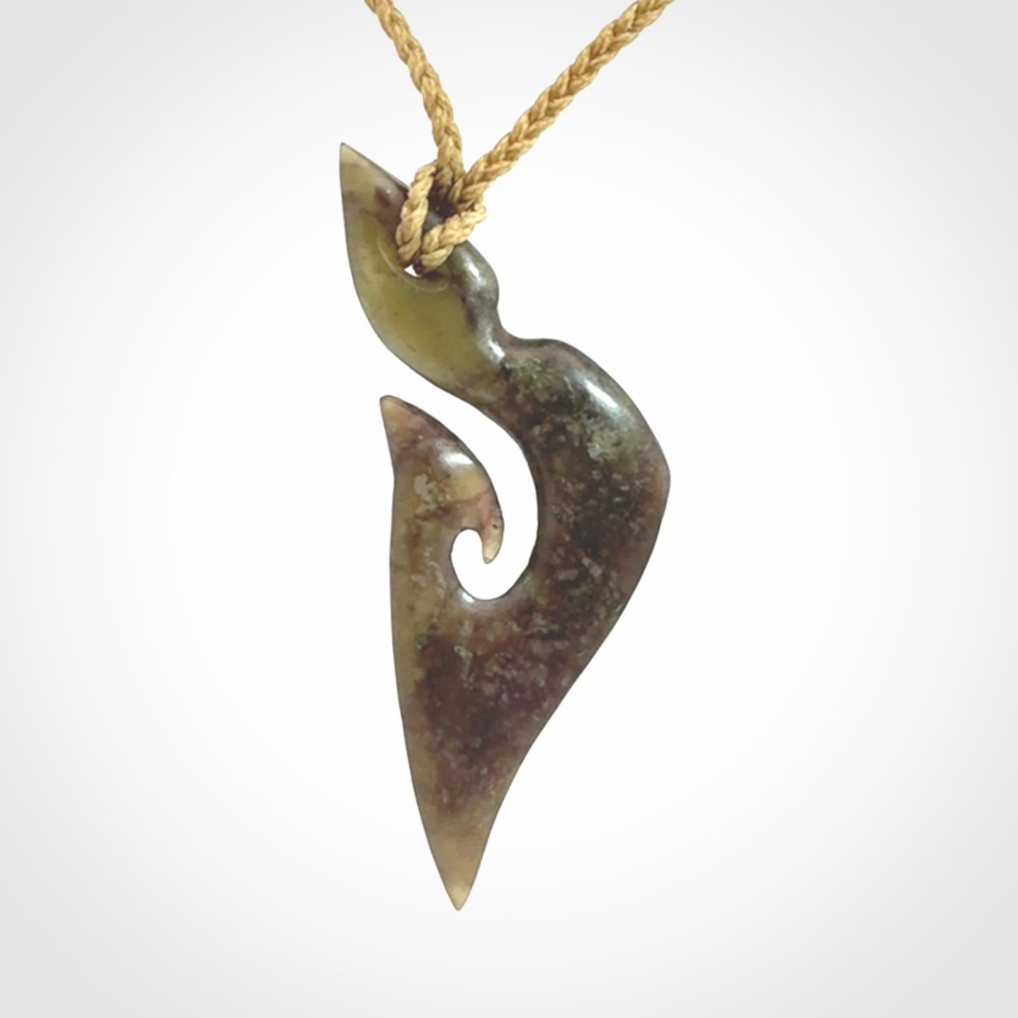 This photo shows a matau, hook, pendant carved from New Zealand Totoweka Pounamu, Jade. We provide this piece with an tan fixed length cord.
