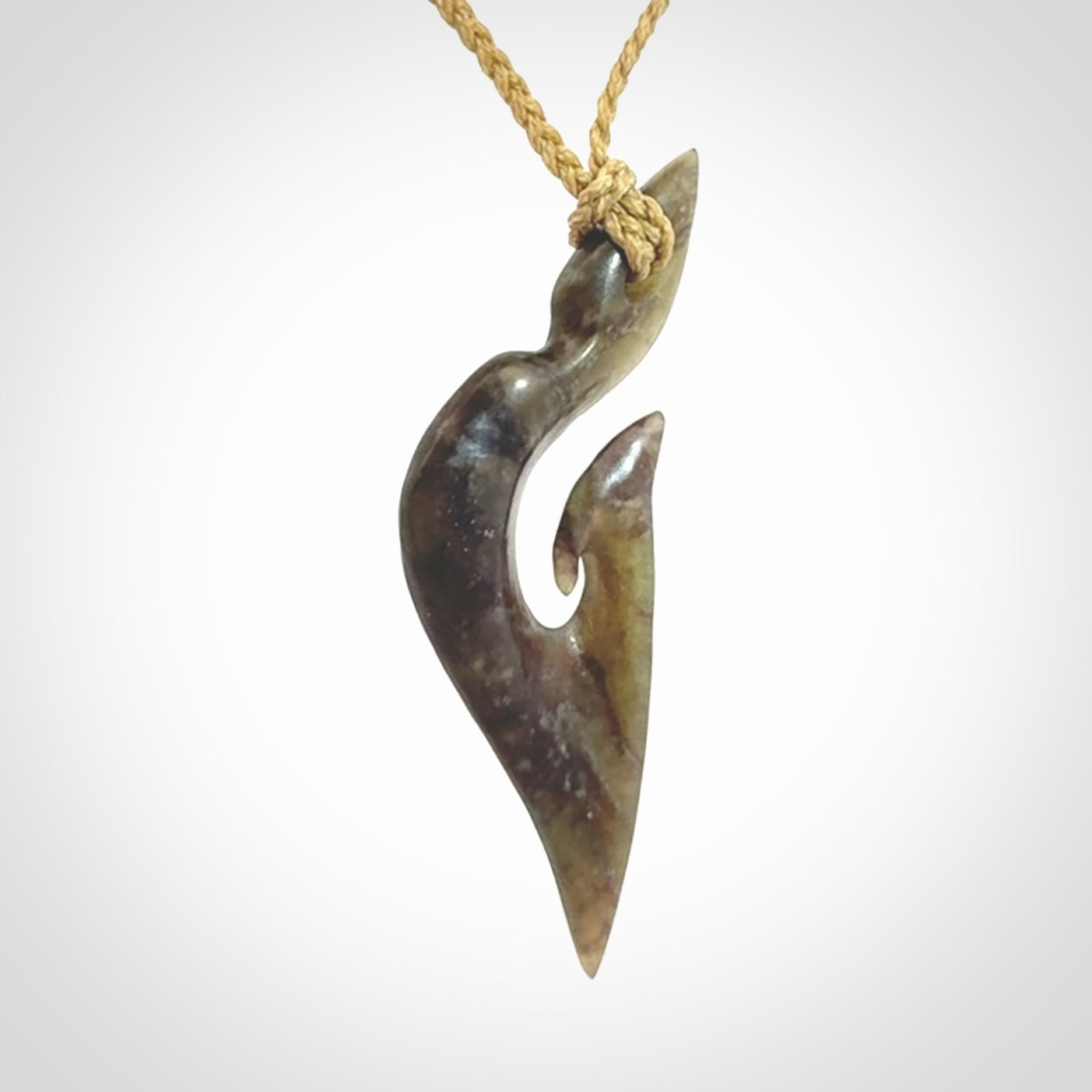 This photo shows a matau, hook, pendant carved from New Zealand Totoweka Pounamu, Jade. We provide this piece with an tan fixed length cord.