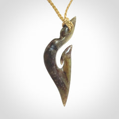 This photo shows a matau, hook, pendant carved from New Zealand Totoweka Pounamu, Jade. We provide this piece with an tan fixed length cord.