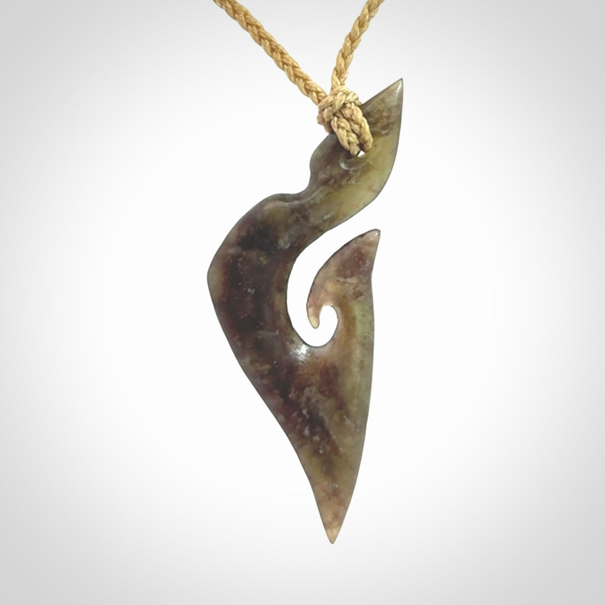 This photo shows a matau, hook, pendant carved from New Zealand Totoweka Pounamu, Jade. We provide this piece with an tan fixed length cord.