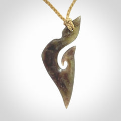 This photo shows a matau, hook, pendant carved from New Zealand Totoweka Pounamu, Jade. We provide this piece with an tan fixed length cord.