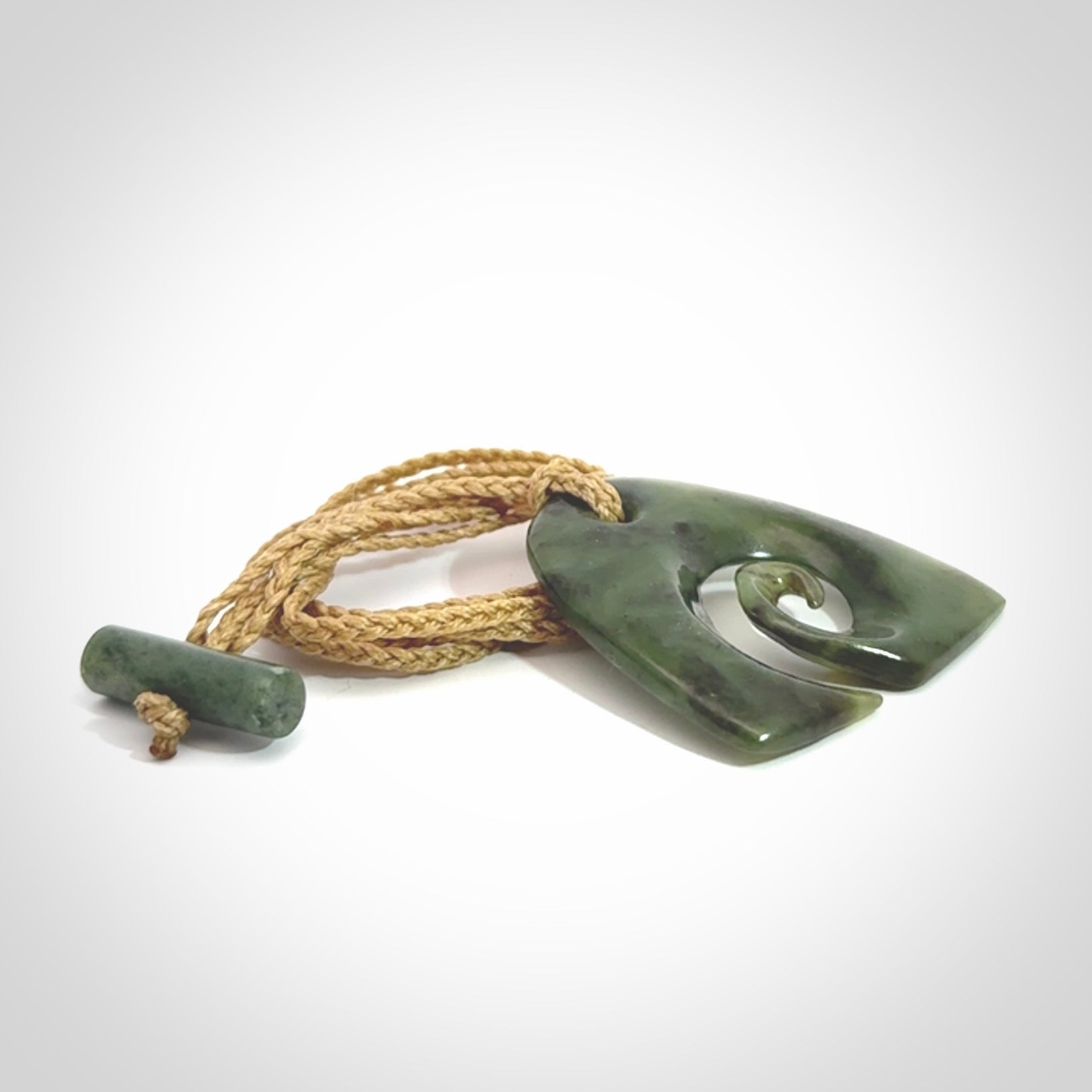 This photo shows a contemporary koru pendant carved from New Zealand Jade. We provide this piece with a tan fixed length cord.