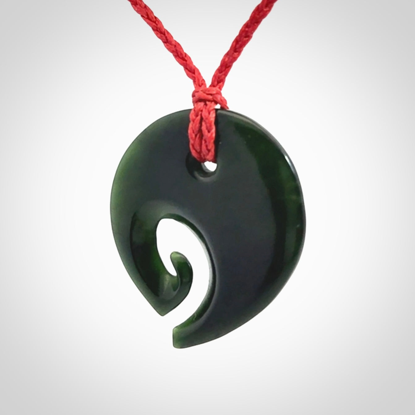 This photo shows a koru pendant carved from New Zealand Jade. We provide this piece with an adjustable red cord.