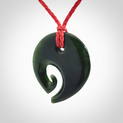 This photo shows a koru pendant carved from New Zealand Jade. We provide this piece with an adjustable red cord.