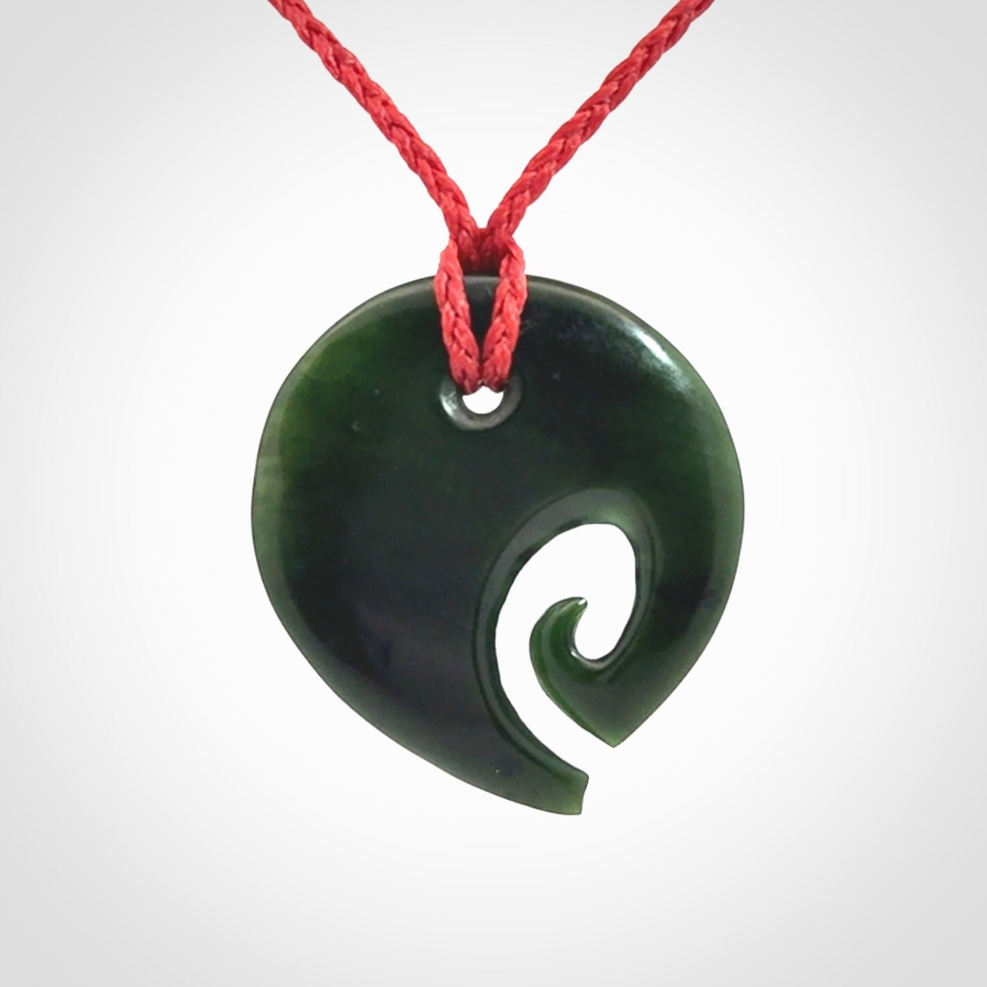 This photo shows a koru pendant carved from New Zealand Jade. We provide this piece with an adjustable red cord.