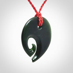 This photo shows a koru pendant carved from New Zealand Jade. We provide this piece with an adjustable red cord.