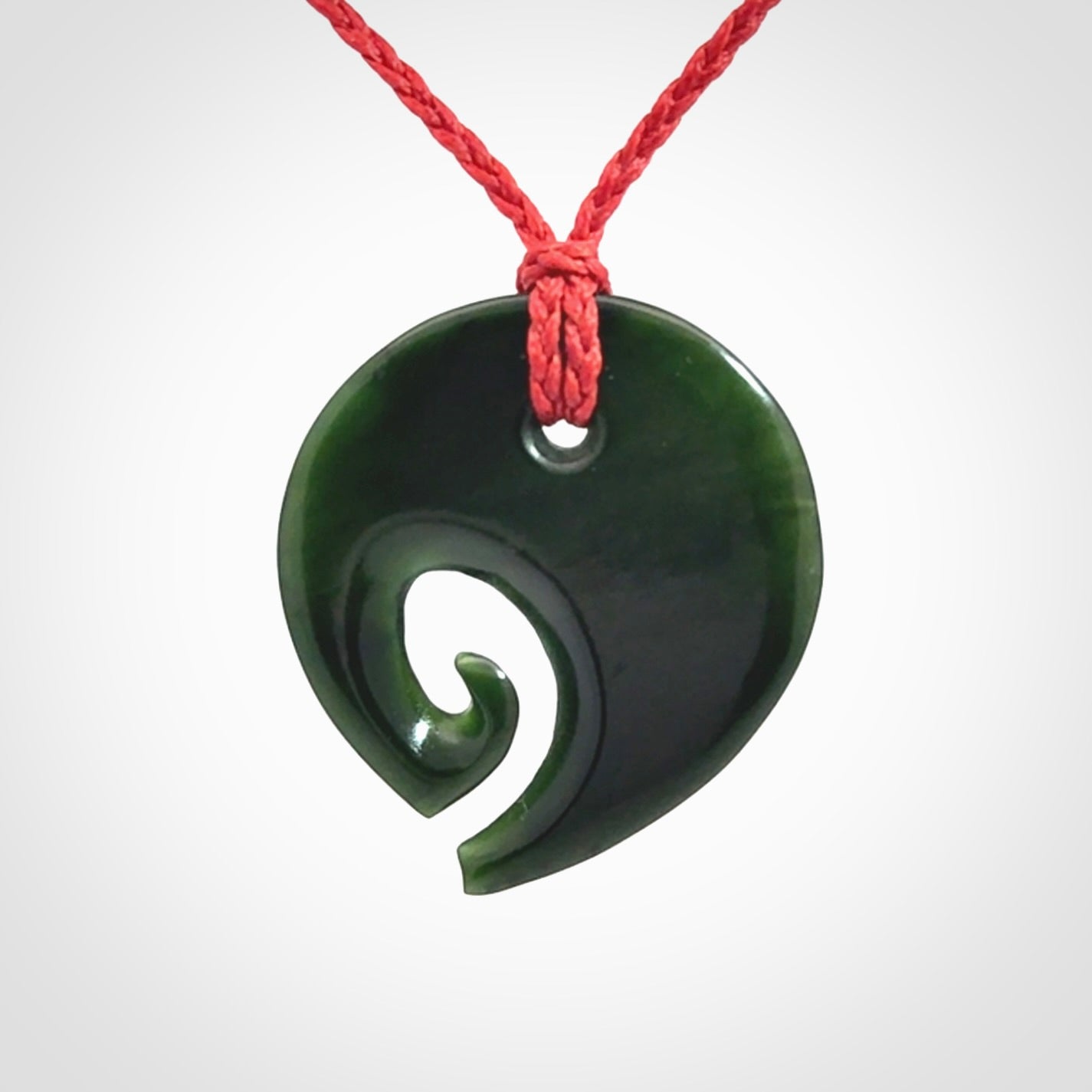 This photo shows a koru pendant carved from New Zealand Jade. We provide this piece with an adjustable red cord.