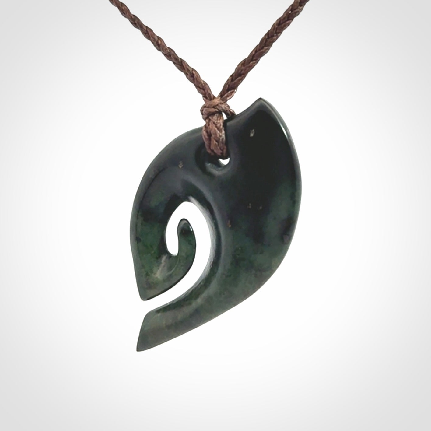 This photo shows a koru pendant carved from New Zealand Jade. We provide this piece with an adjustable brown cord.