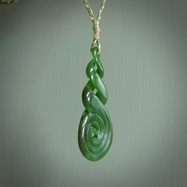 Ross Crump triple twist with koru pendant. Hand carved from rare New Zealand jade this is a beautiful pounamu pendant. The cord is hand plaited in green and white colours and is length adjustable. It has a floret in white. It is a delicate and very beautiful greenstone pendant. For sale online by NZ Pacific.