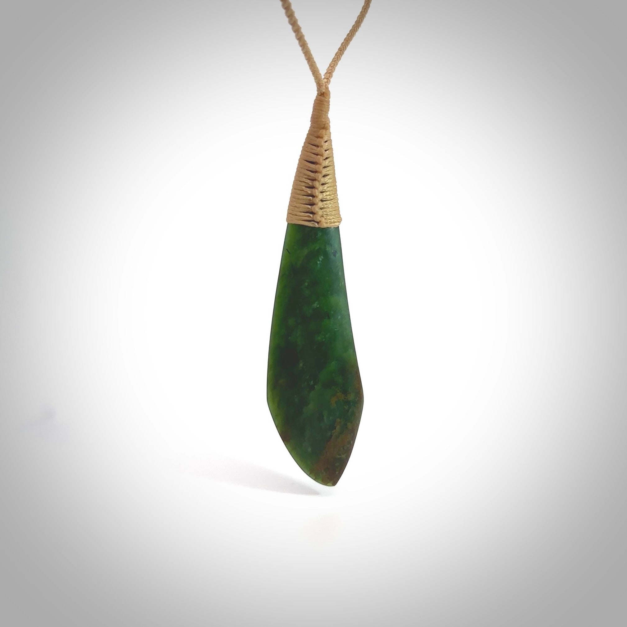 This photo shows a beautiful large jade drop. It is handcarved from a piece of green New Zealand pounamu, with fascinating light green inclusions throughout the stone. We have this on a creme coloured, adjustable four plait cord. We ship this worldwide with an express courier service. Postage is free.