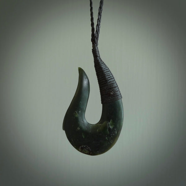 This photo shows a greenstone hook, or matau, pendant. It is a beautiful deep green jade. The cord is plaited black and the length can be adjusted.