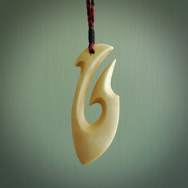 This is a larger bone hook, or matau, pendant carved from a piece of bone. The cord is a black and red colour and the length of the cord can be adjusted. It is a large sized pendant and is well carved. A beautiful piece of traditional jewellery.