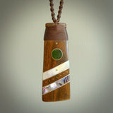 This photo shows a medium sized Toki pendant hand carved from lignum vitae with New Zealand Pounamu Jade, Mother of Pearl and Paua Shell inlay alongside; brass and silver. This is a stand out one off necklace for those who appreciate art to wear. It is provided with a cord in brown that is a fixed length with Paua Shell Toggle. We ship this piece worldwide and shipping is included in the price.