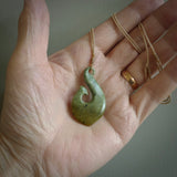 This picture shows a jade hook pendant, also called a hei-matau, carved for us in New Zealand jade. The jade is a wonderful deep mint green pounamu. This is a rare jade loved and valued for its distinctive colour. The carver is Ric Moor - and this is a beautiful example of his work. The cord is a four-plait, adjustable brown coloured necklace.
