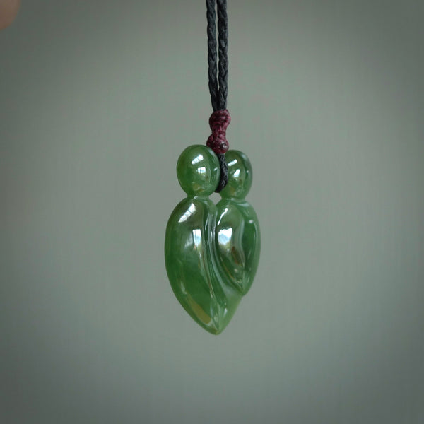This picture shows a stylised couple in a close embrace sharing a kiss. The pendant is hand carved from a bright tree, faultless piece of British Columbian jade. The cord is a 3-ply plaited black with a plum coloured floret.