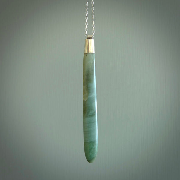 This picture shows a hand carved Inanga Pounamu, jade drop pendant with sterling silver cap and chain. The jade is a very dark green with a shimmer of light blue tones in the stone. It is suspended from a sterling silver clasp and we supply a sterling silver chain. Delivery is free worldwide.