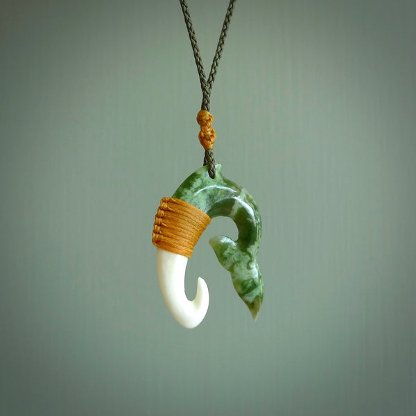 This photo shows a beautiful jade whaletail with bone pendant. It is handcarved from a piece of mottled green Jade, with fascinating mauve tinges through the stone. We have this on a burnt gold and flax coloured, adjustable cord with a burnt gold green floret just above the pendant and binding. We ship this worldwide with an express courier service. Postage is free.