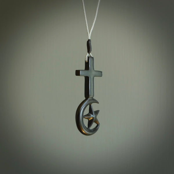 This pendant is a series of religious symbols carved in one piece of black jade. The top is a christian cross and at the bottom is the crescent of islam. It is suspended on a snowstorm grey plaited cord which is length adjustable.
