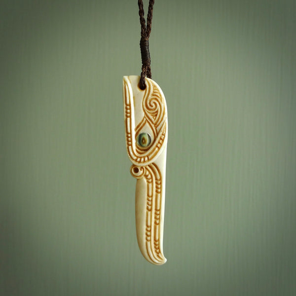 This picture shows a carved kāhu, hawk in bone. It is a drop shaped pendant. The artist has carved traditional decorative kowhaiwhai designs into the body and these run up the sides of the hawk. These have specific meanings. It is provided with a hand-plaited brown cord that is length adjustable. Shipping is included and we ship worldwide.