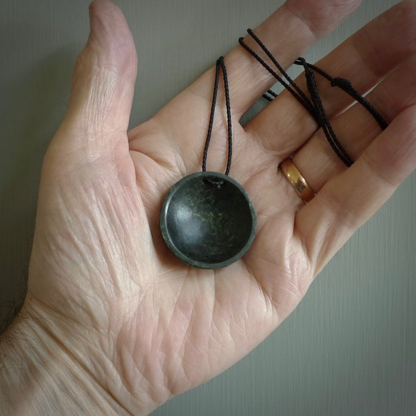 This piece is a oval round, disc pendant. It was carved for us by Ric Moor from a lovely light and milky green piece of New Zealand jade. It is suspended on a black coloured braided cord that is length adjustable.