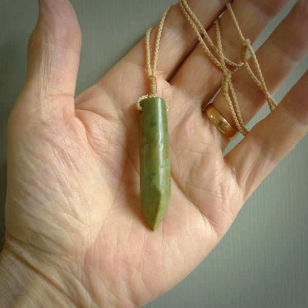 This picture shows a hand carved flower jade drop pendant by Ric Moor. The jade is a wonderful green with a shimmer of orange tones in the stone. It is suspended from a beige adjustable cord. Delivery is free worldwide.