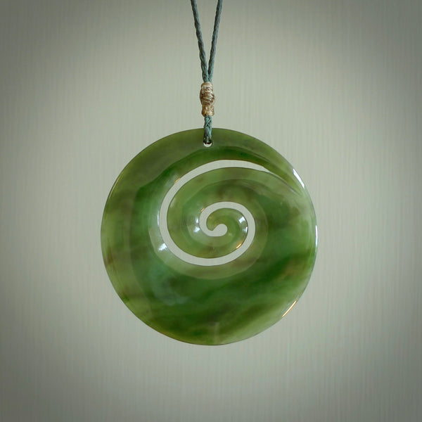 This picture shows a large hand-carved koru. It is carved from British Columbian jade and is suspended from a hand-plaited, black cord. Free delivery worldwide. BC Jade koru necklace.