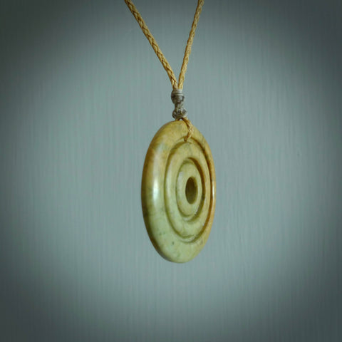 This picture shows a hand carved disc pendant made from a bright orange and green coloured flower jade. The front face is a unique design and the back is flat. It is provided with an adjustable kowhai yellow cord.