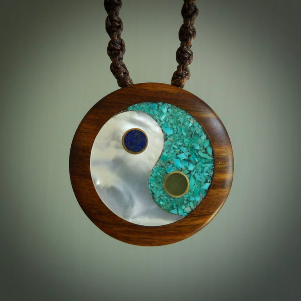 This photo shows a medium sized yin and yang pendant hand carved from lignum vitae with New Zealand Pounamu Jade, Lapis Lazuli, Mother of Pearl and Paua Shell inlay alongside; brass and silver. This is a stand out one off necklace for those who appreciate art to wear. It is provided with a cord in brown that is a fixed length with Paua Shell Toggle. We ship this piece worldwide and shipping is included in the price.