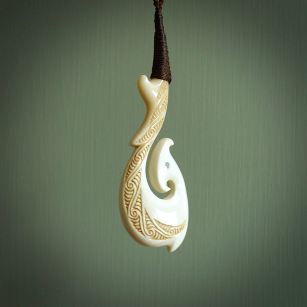 This picture shows a carved hook in bone. The artist has carved traditional decorative kowhaiwhai designs into the body and these run up the insides of the matau. These have specific meanings. It is provided with a hand-plaited brown cord that is length adjustable. Free shipping worldwide.