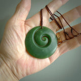 This picture shows a large hand carved jade koru pendant. It is a darker green colour which is quite translucent where the jade is thin. Although a large piece, it is a wonderful, delicate piece of jewellery. The cord is hand plaited and adjustable so that you can position the pendant where it suits you best. This koru was carved for us by Ric Moor. Delivery is free worldwide.